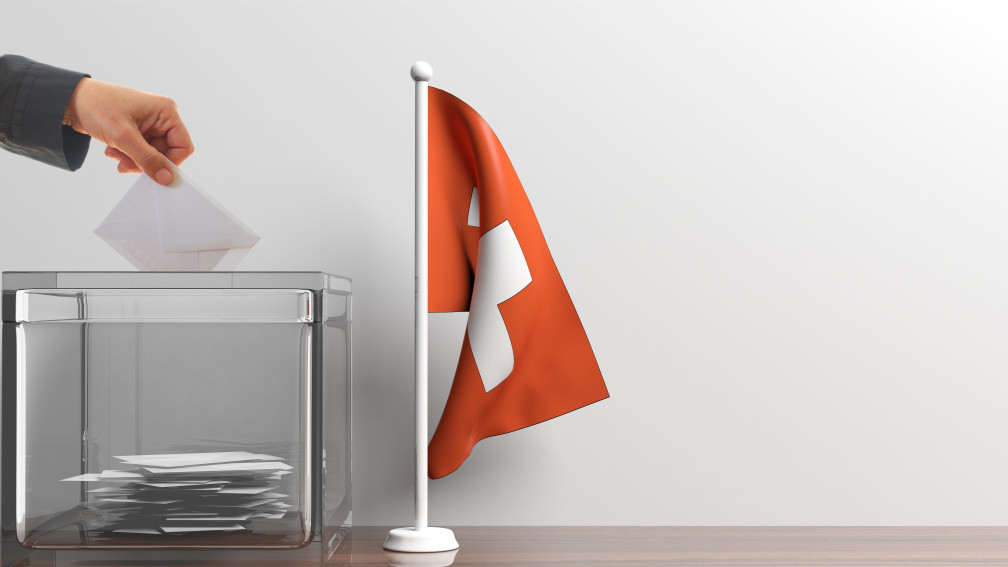 Wahlurne und eine Schweizer Flagge daneben