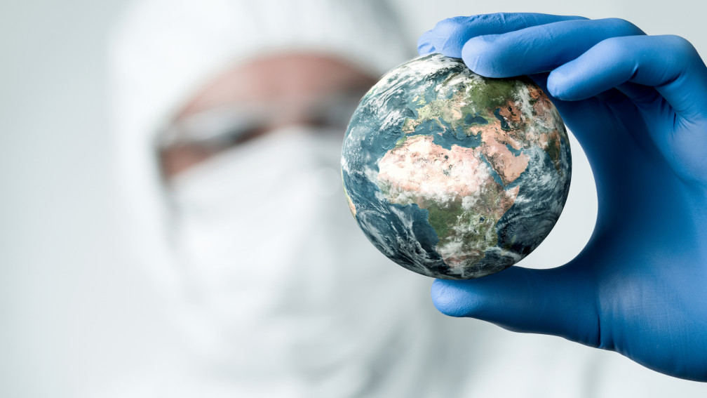 Forscher mit Gesichtsmaske hält Globus in einer Hand