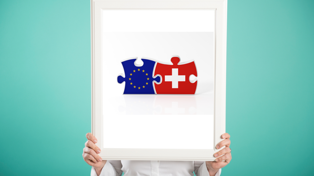 Une personne tient un cadre avec une image: deux pièces de puzzle emboîtées; l'une représentant l'UE l'autre la Suisse