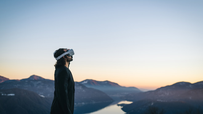 Person mit Virtual Reality Brille schaut ins Weite Hintergrund See und Gebirge