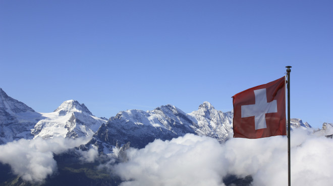 Wolkenverhangene Bergspitzen mit wehender Schweizer Fahne