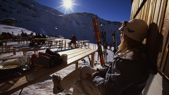 Frau sitzt mit Skiausrüstung vor Skihütte