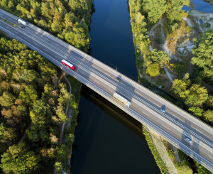 Lastwagen fahren über Brücke; darunter Wälder und ein Fluss