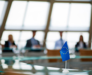 Kleine Europafahne im Fokus im Vordergrund, im Hintergrund Politiker am Tisch