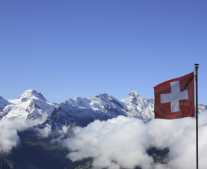 Wolkenverhangene Bergspitzen mit wehender Schweizer Fahne