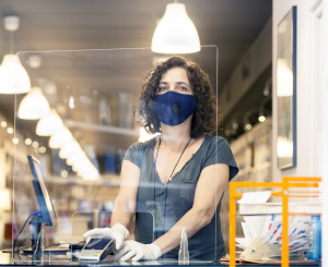 Verkäuferin mit Mundschutz hinter einer Plexiglasscheibe